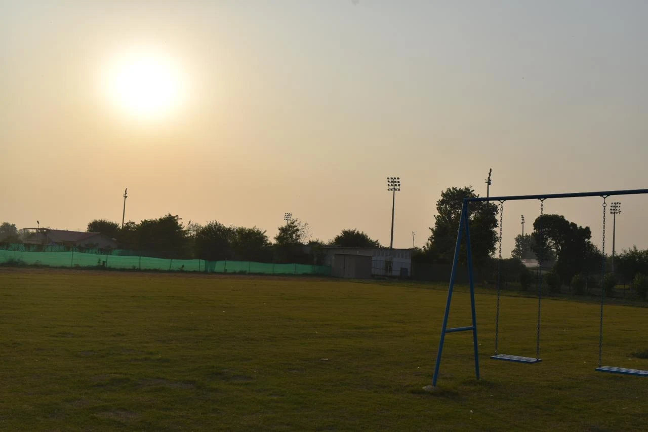 Empty playground swings on green grass field with setting sun at WildOoks Animal Petting Farm Sector 134 Noida