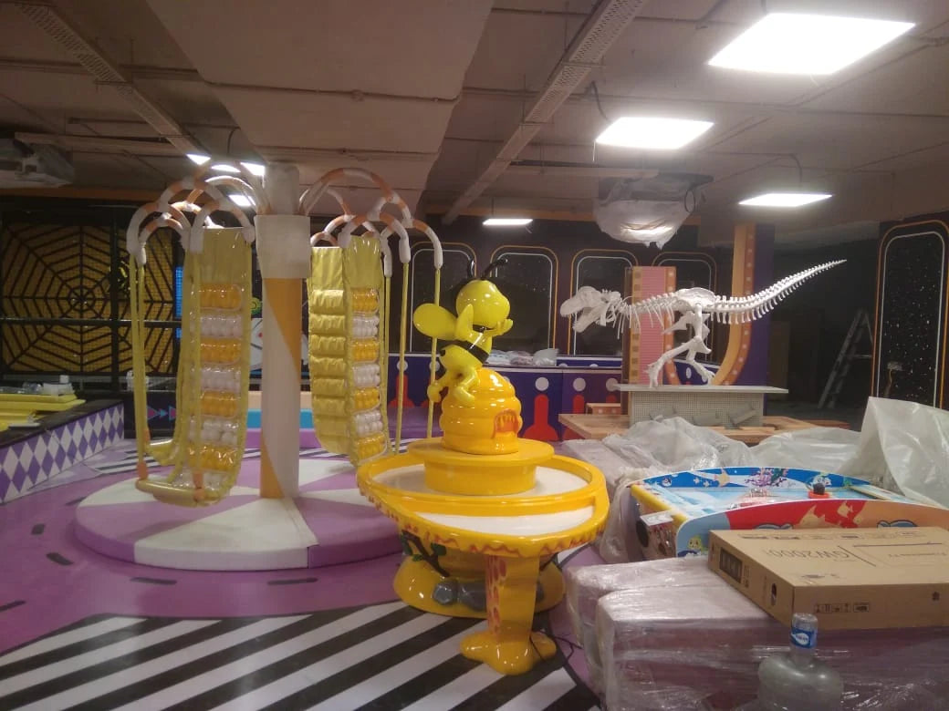 An indoor amusement park under construction with colorful rides and a dinosaur skeleton.