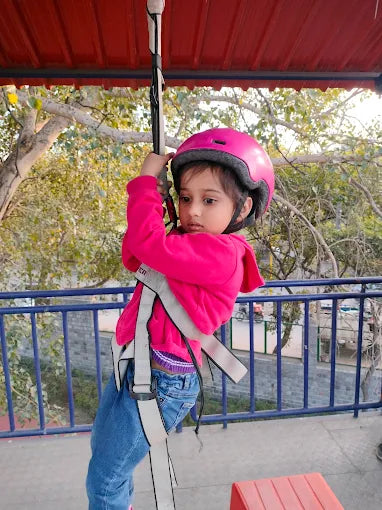 Young girl wearing pink helmet and jacket harnessed for zip-lining at Extreme by Tingaland Punjabi Bagh Delhi