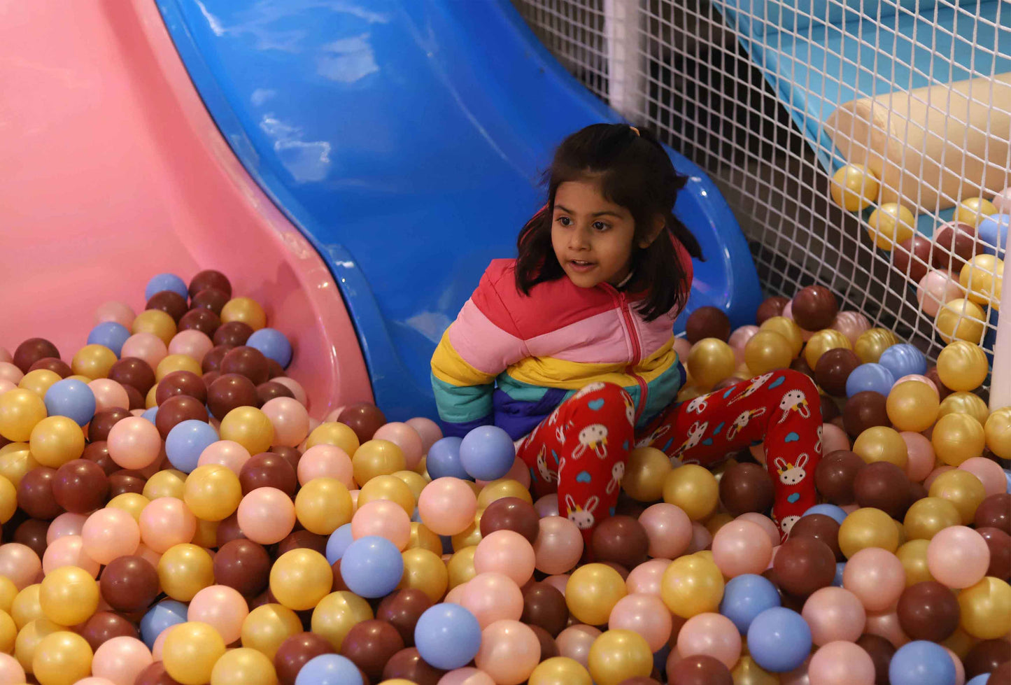 Young girl enjoying a colorful ball pit next to a blue slide in a lively indoor play area at Zig Zag Zoh Faridabad