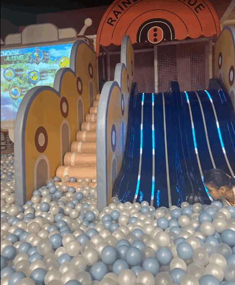 Indoor play zone with three dark slides and beige stairs leading into a pastel-colored ball pit at Zig Zag Zoh Gurgaon