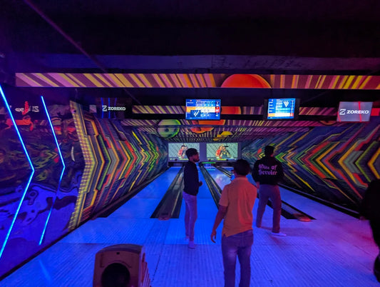 Young adults bowling in a neon-lit alley with colorful, abstract graphics on the walls.