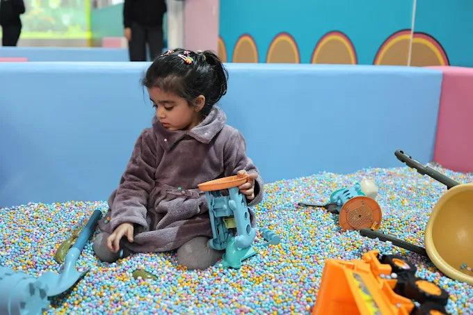 A young girl plays with toys in a ball pit.