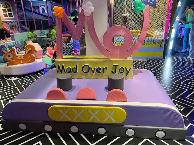 A colorful play area with children and a large "Mad Over Joy" sign.