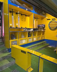 A brightly lit yellow and blue sports shop displays cricket bats and gear on shelves.