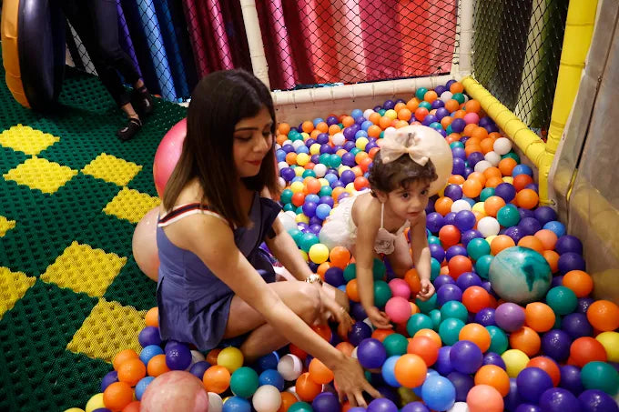 A woman and a young child play in a ball pit filled with colorful balls.