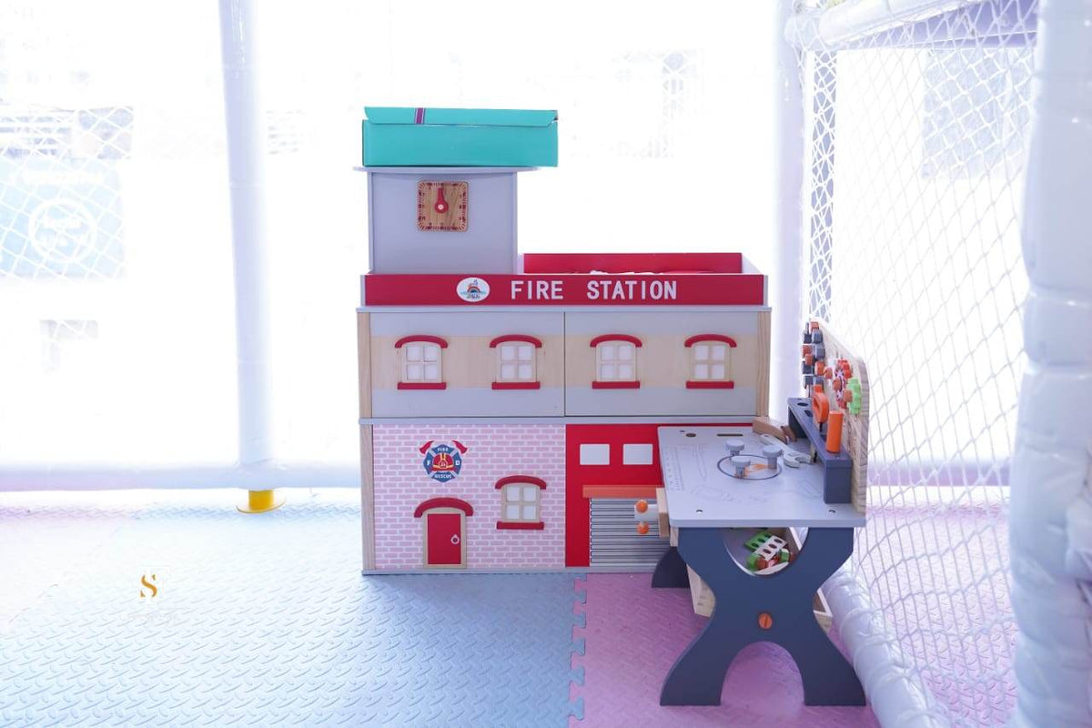 A wooden toy fire station and workbench in a playroom.