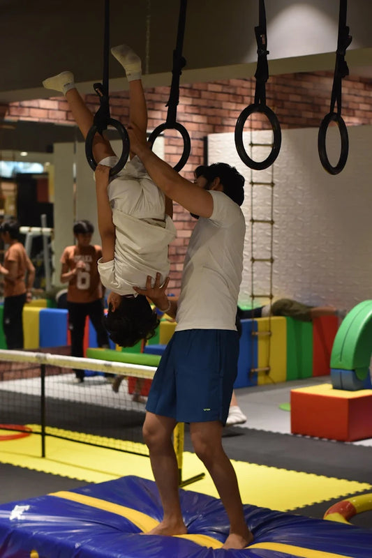 A man helps a child doing a gymnastic exercise on rings in a gym.
