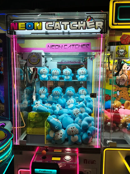 A claw machine filled with blue Doraemon plush toys, with "NEON CATCHER" lit up above.