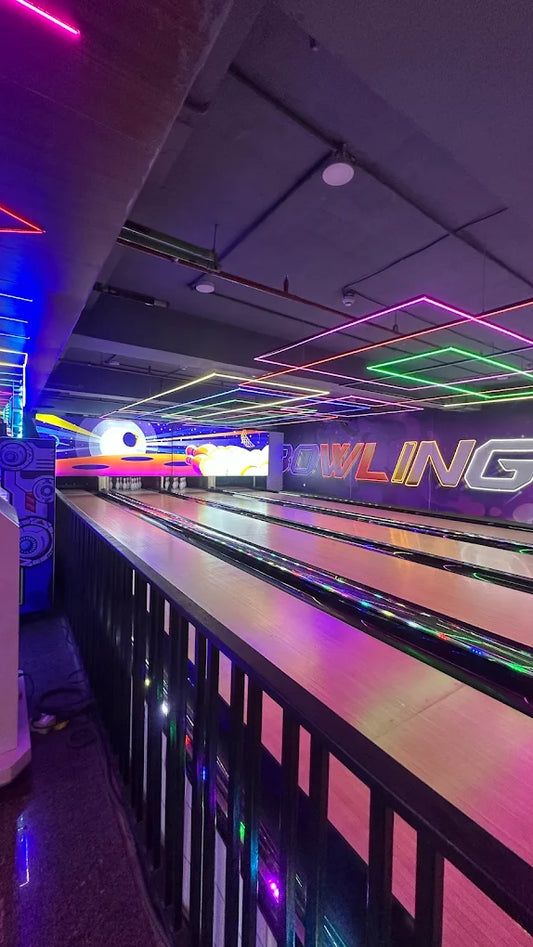 A bowling alley with neon lights and a colorful digital screen displaying the word "BOWLING."
