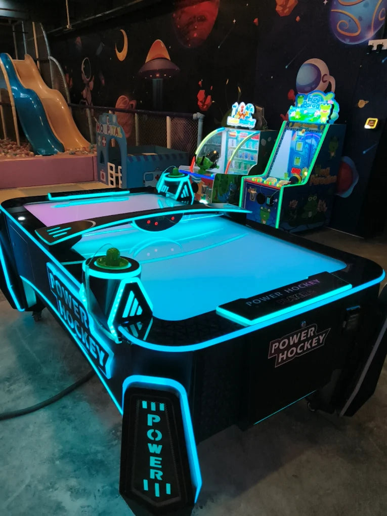 An air hockey table glows with blue lights in an arcade with space-themed decor.