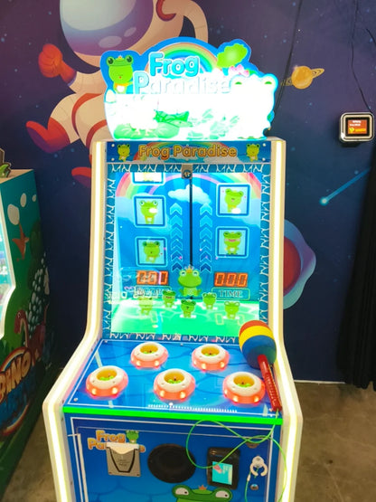 A children's arcade game called "Frog Paradise" with a colorful mallet and illuminated targets.