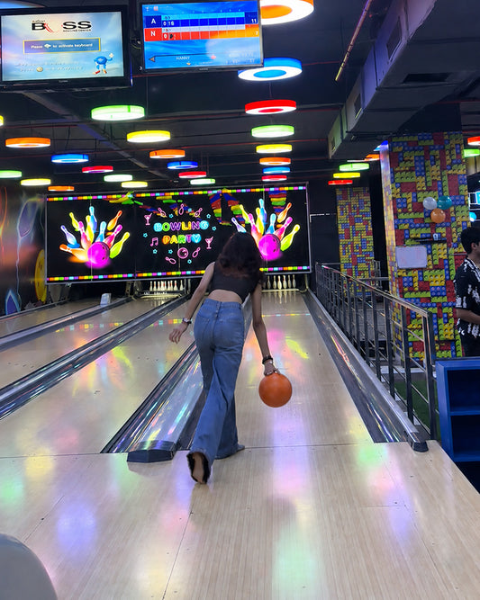 A young woman bowls an orange ball down a colorful lane at a bowling alley.
