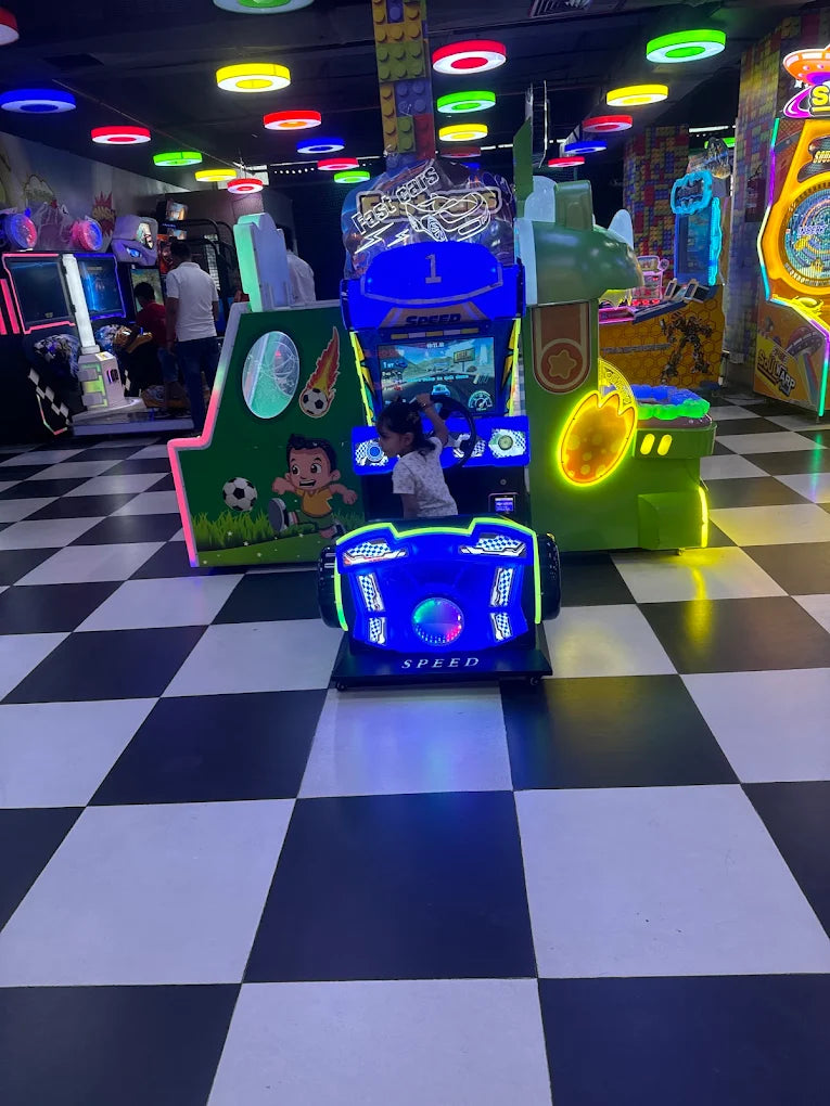 A young child plays a racing arcade game in a brightly lit amusement center.