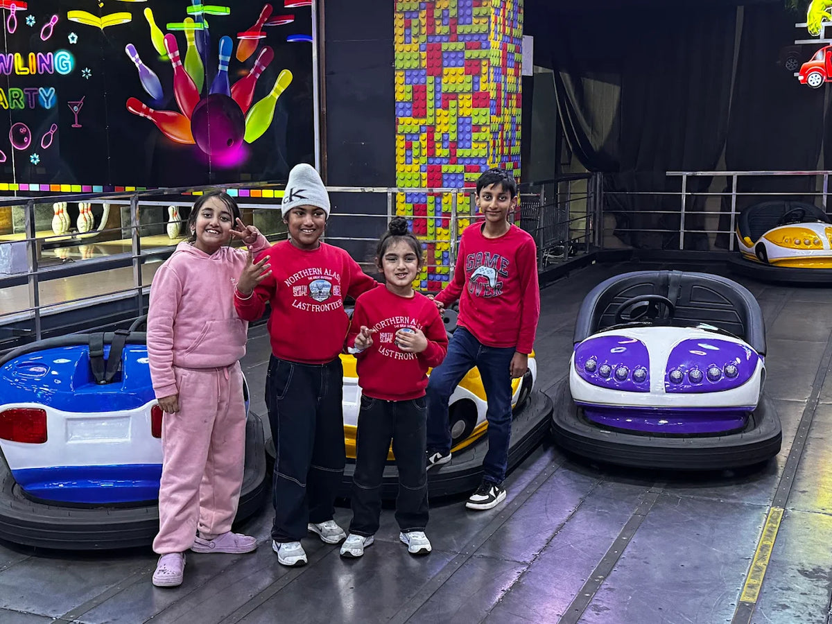 Children pose in front of bumper cars at an amusement park with a bowling-themed backdrop.