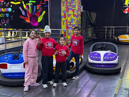 Children pose in front of bumper cars at an amusement park with a bowling-themed backdrop.