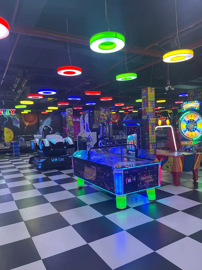An arcade with colorful lights and games, including a VR car and air hockey table.