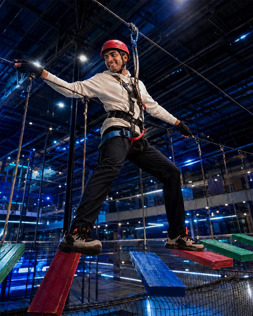 A young person navigates a challenging ropes course, balancing on colorful wooden planks suspended in the air.