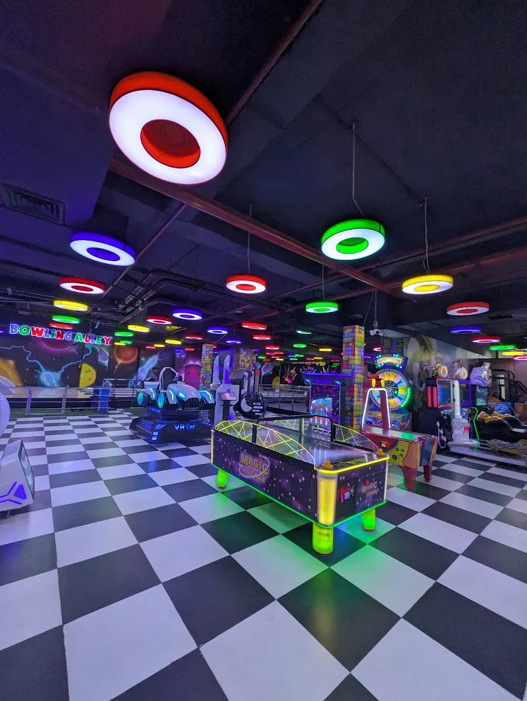 An arcade with a checkered floor, colorful lights, and various games like air hockey and VR rides.