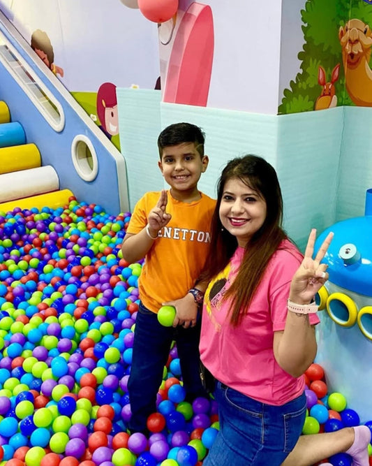 A boy and a woman pose in a ball pit at an indoor playground.