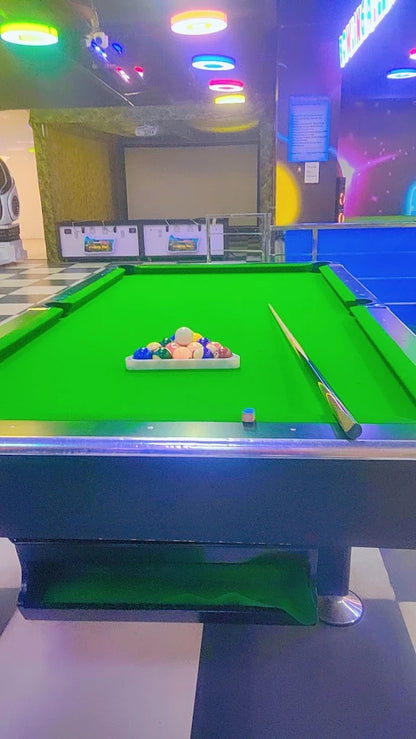 A billiard table with balls racked and a cue stick on the green felt.