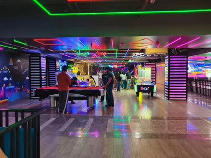 People play pool and arcade games in a brightly lit entertainment center with neon lights.