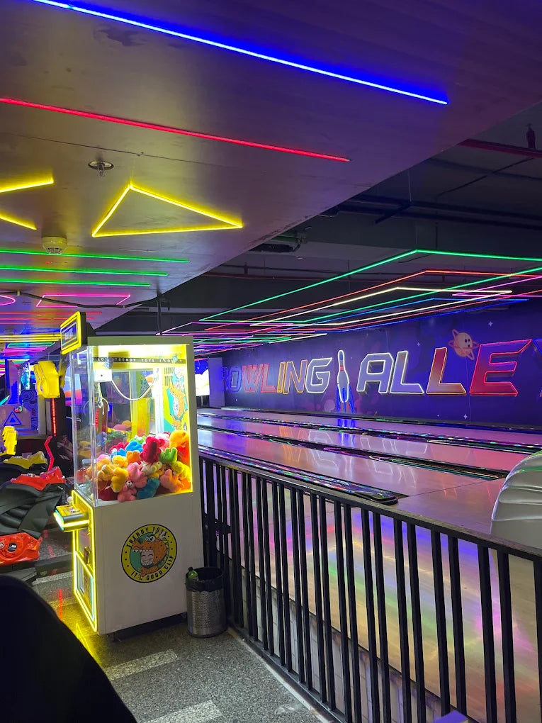 A neon-lit bowling alley with arcade games and bowling lanes.