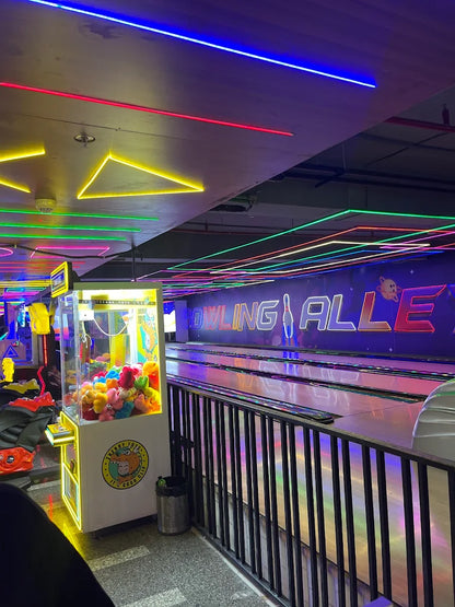 A neon-lit bowling alley with arcade games and bowling lanes.