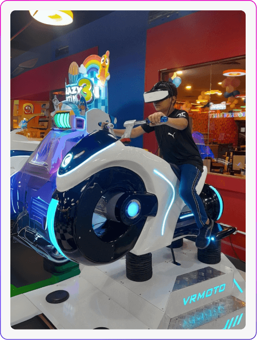 A young person plays a VR motorcycle game in an arcade. The game features a futuristic white motorcycle with blue lights.