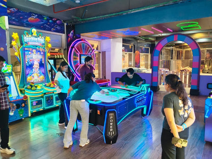 Young adults play air hockey and other arcade games in a brightly lit entertainment center.