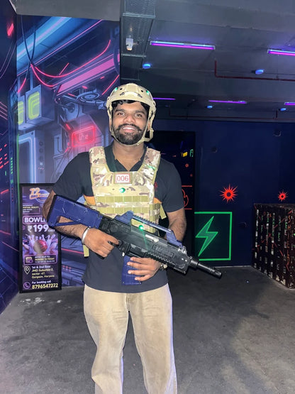 A young man in a tactical vest and helmet holds a toy rifle in a neon-lit laser tag arena.