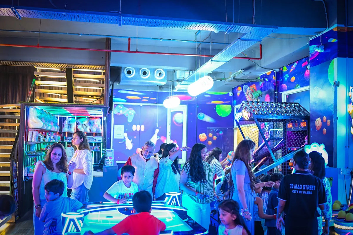 A group of adults and children enjoy arcade games in a brightly lit, neon-colored entertainment center.