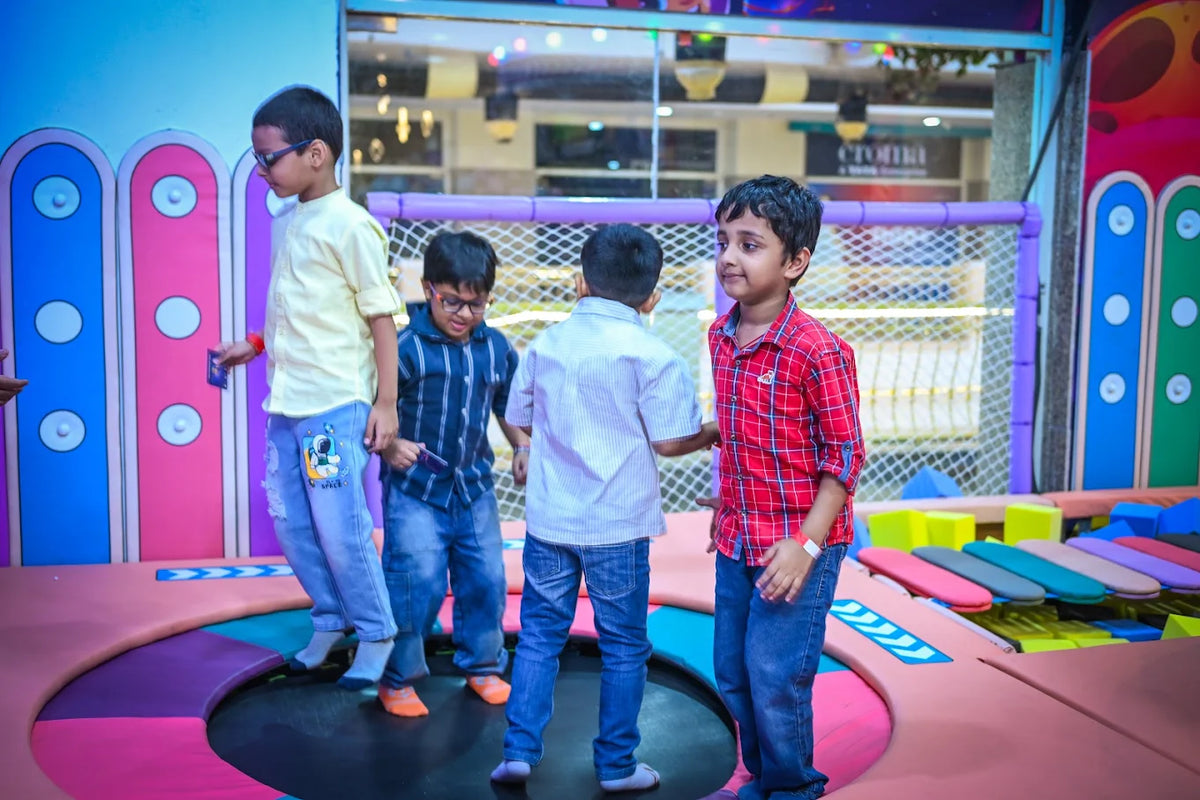 Four young boys are playing on a trampoline in an indoor play area.