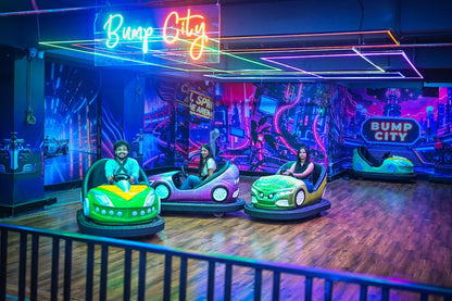 Young adults enjoy bumper cars in a neon-lit arcade with a cityscape mural.