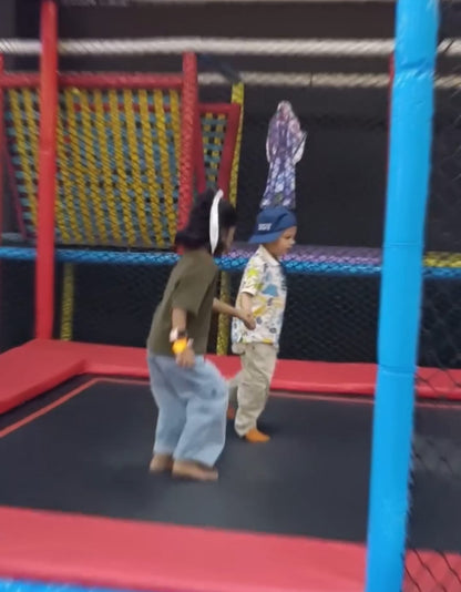 Two young children are jumping on a trampoline in an indoor play area.