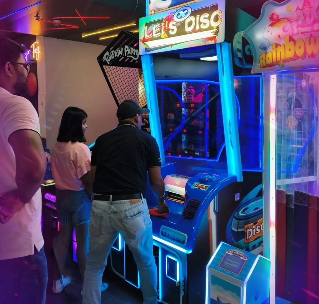 Adults play an arcade game called "Let's Disc" in a brightly lit entertainment center.