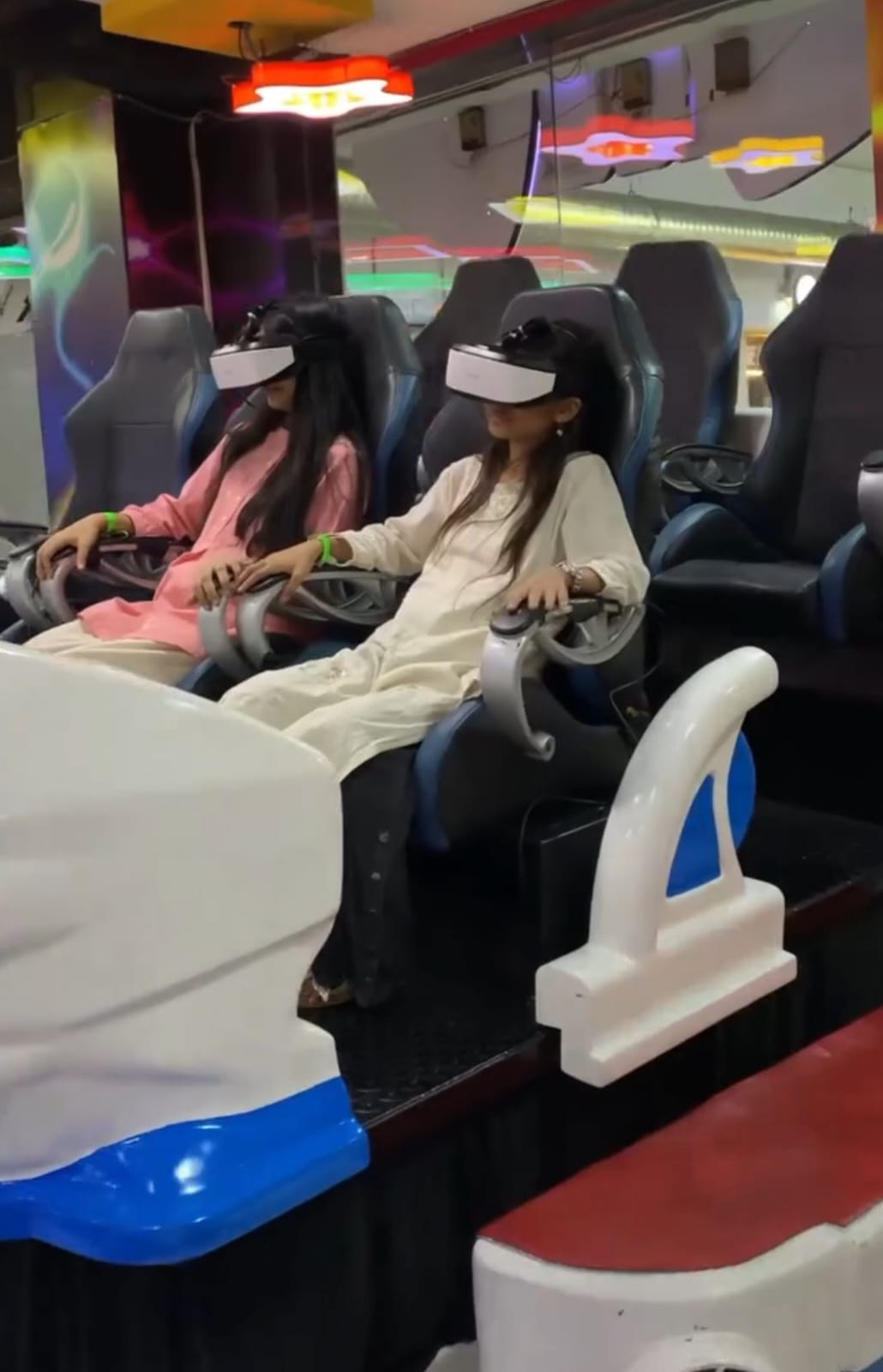 Two young girls wearing VR headsets sit in a virtual reality simulator ride.