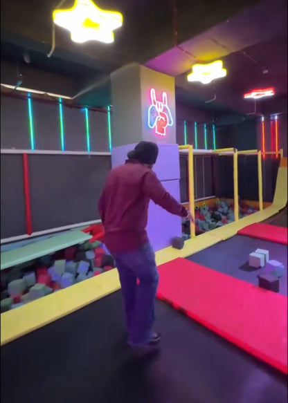 A person jumps on a trampoline in a colorful indoor play area with foam pits and neon lights.