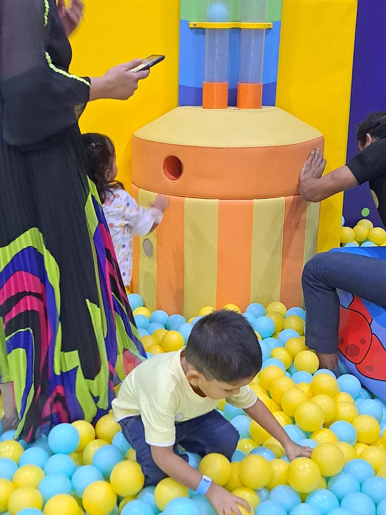 A young boy plays in a ball pit while an adult watches.