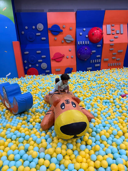 A young child plays in a ball pit with a large inflatable tiger.