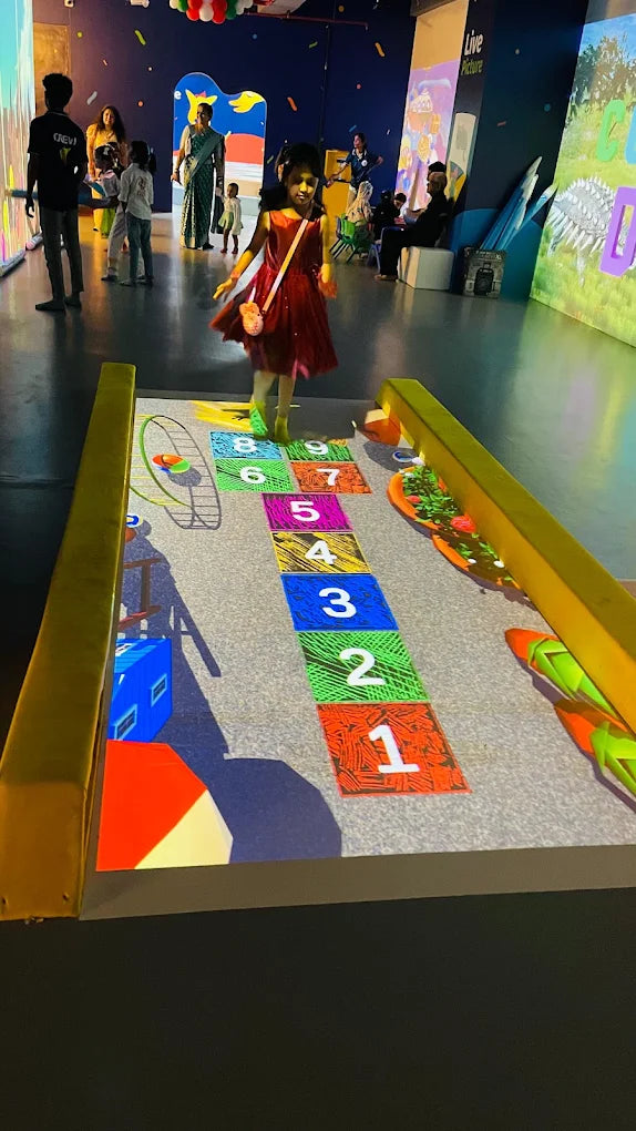 A young girl plays hopscotch projected on the floor in a brightly lit indoor space.