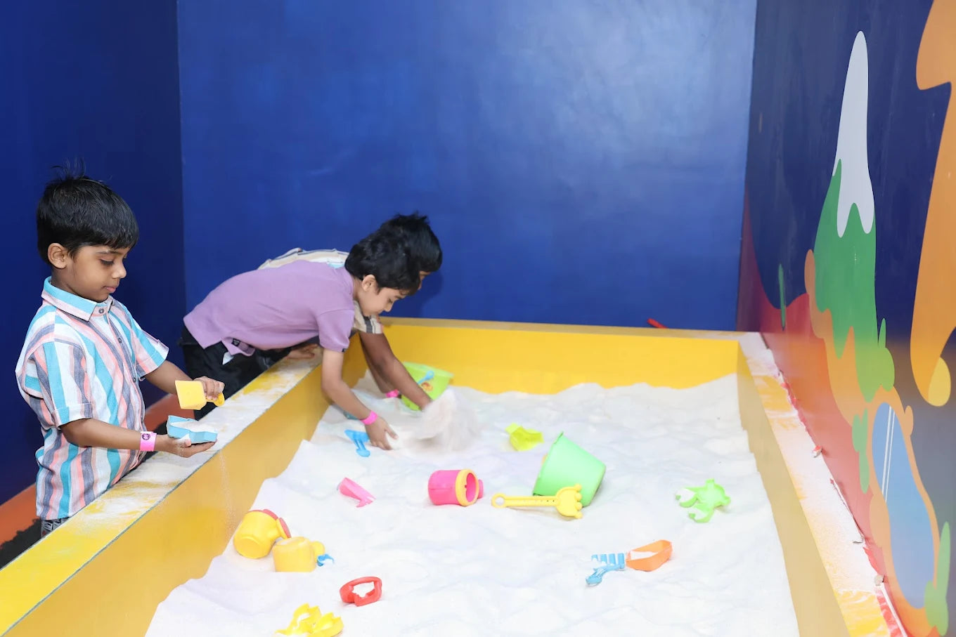 Two young boys play in a sandbox with colorful toys.