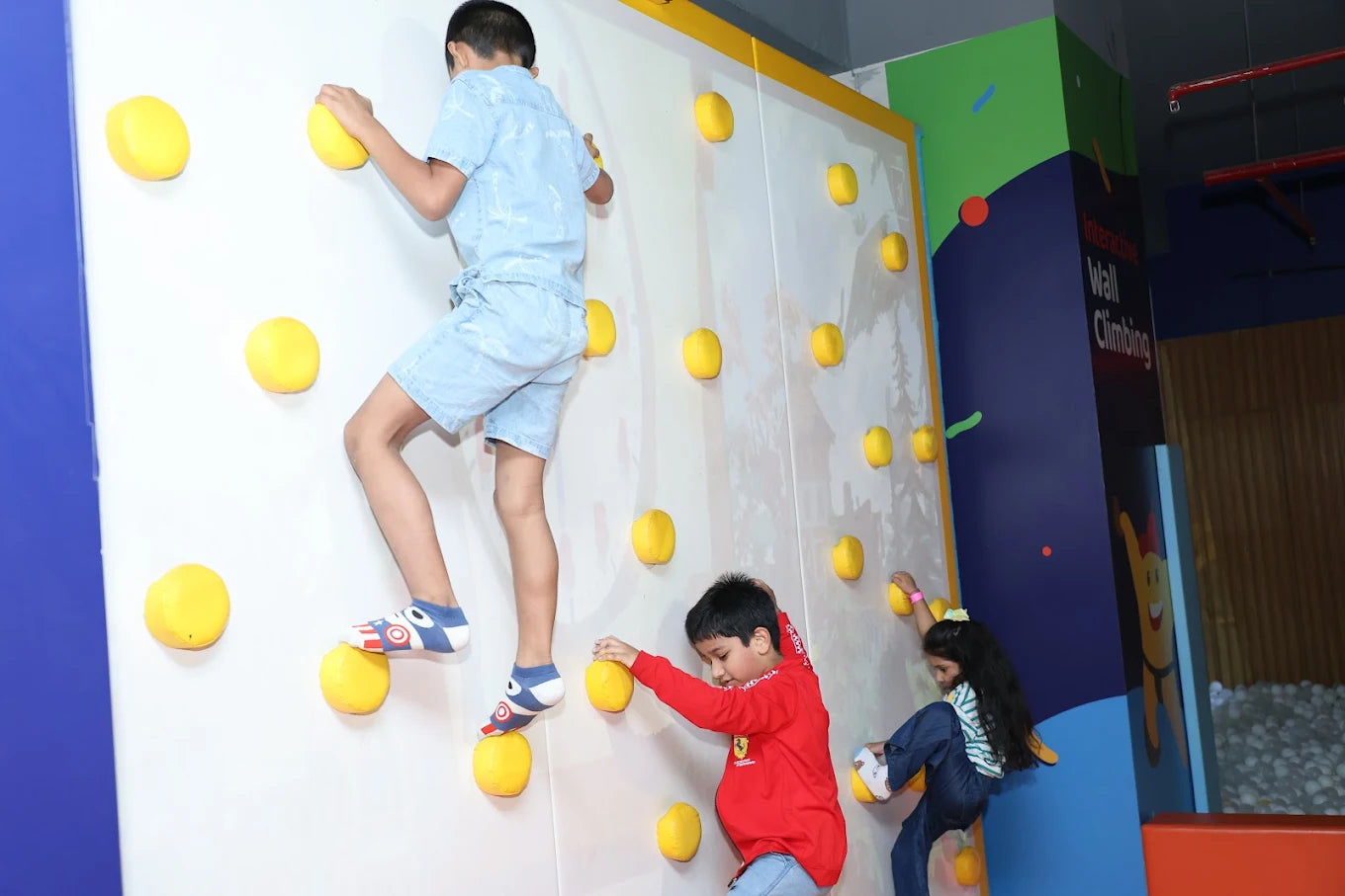 Children climbing a colorful indoor wall with yellow holds.