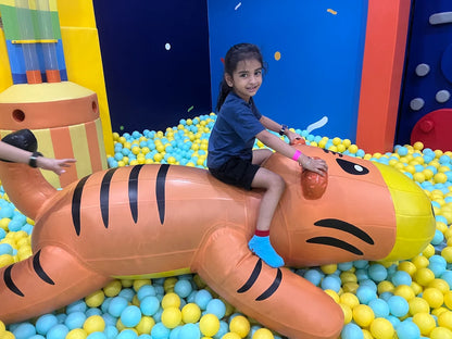 A young girl rides an inflatable tiger in a ball pit.