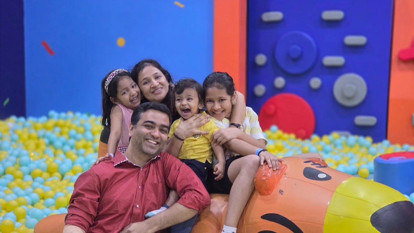A family with young children smiles in a ball pit at an indoor playground.