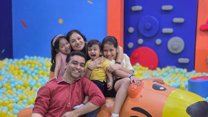 A family with young children smiles in a ball pit at an indoor playground.