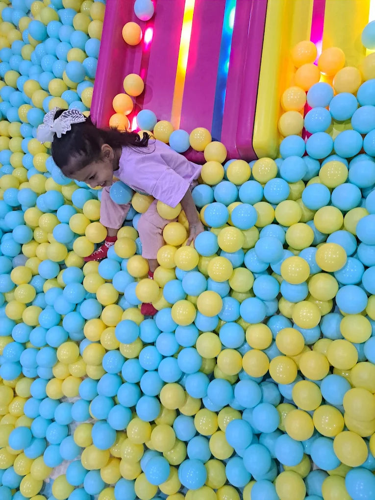 A young girl plays in a ball pit filled with blue and yellow balls.