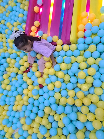 A young girl plays in a ball pit filled with blue and yellow balls.