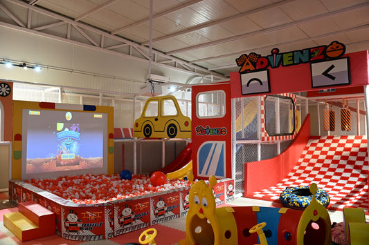 A colorful indoor playground with a ball pit, slides, and a projected game for children.