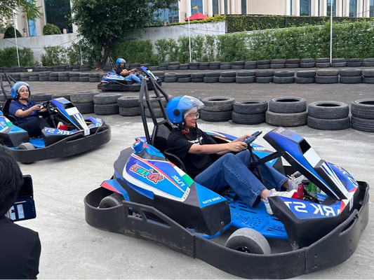 People driving go-karts on a track with a building and trees in the background